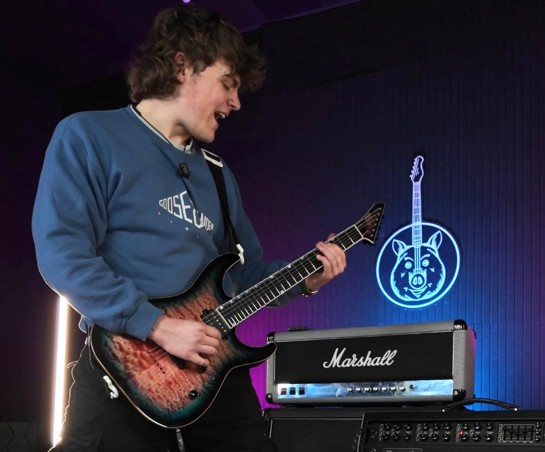 Ben Keightley playing guitar in front of Marshall amplifiers with a blue logo in the background